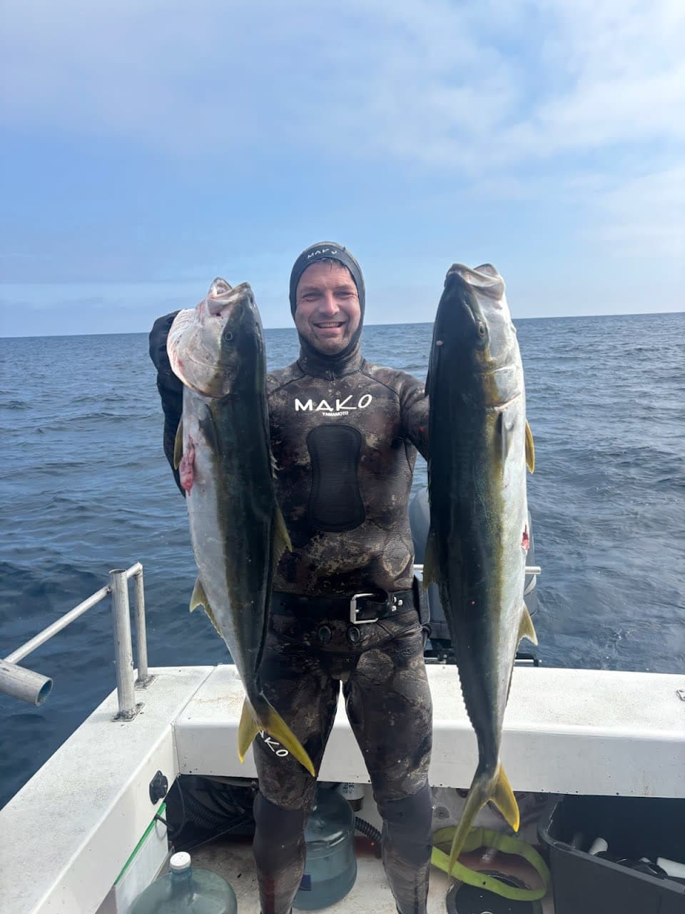 Spearfisherman on a boat deck holding two large California yellowtail.